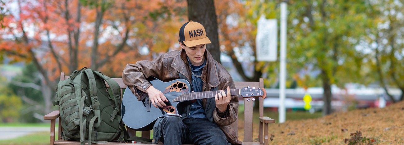 Person playing his guitar on a bench outdoors on a fall day.