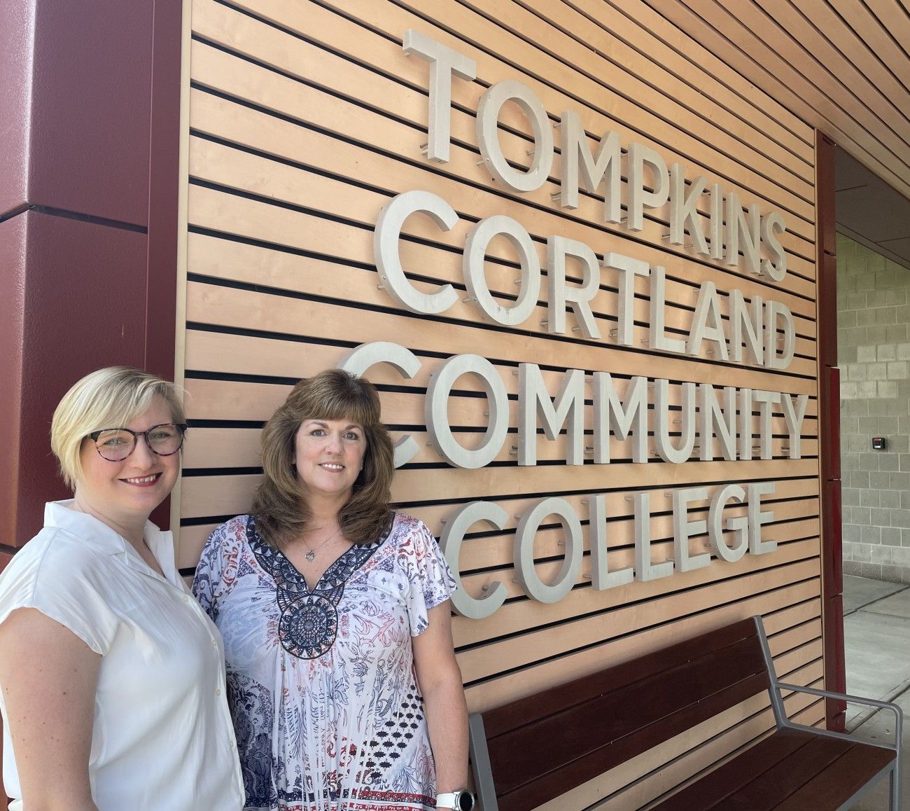 Two women standing in front of a sign that says "Tompkins Cortland Community College"